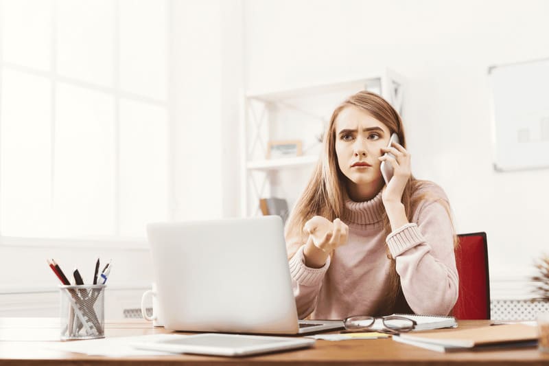 femme mécontente au téléphone devant son ordinateur assise dans son bureau
