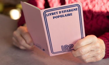 Personne âgée tenant un livret d'épargne populaire entre ses mains